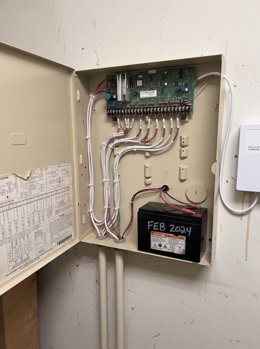 The same panel after takeover: wiring combed into labeled runs, a new battery, and a cellular communicator fitted alongside