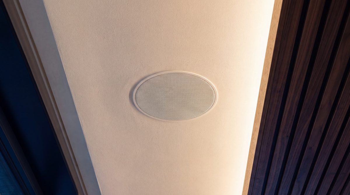A recessed ceiling speaker flush in a plaster ceiling beside walnut slats