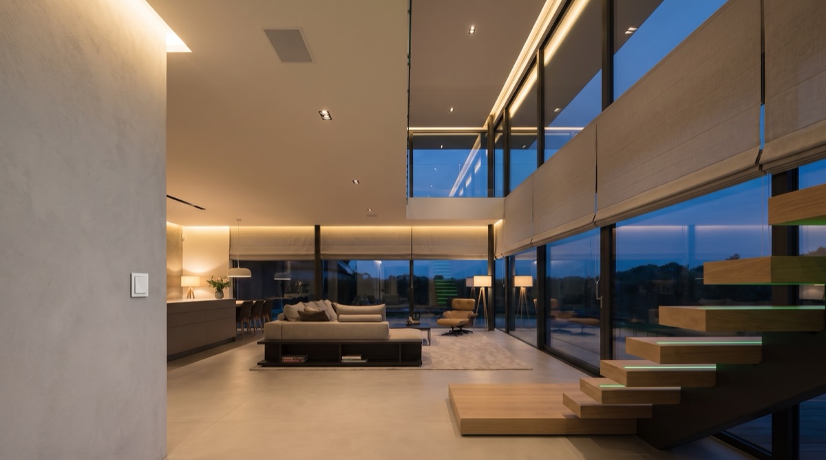 A dusk living space with shades lowering in sync and layered lighting scenes running themselves